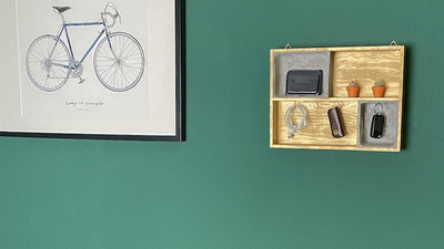 DIY Schlüsselkasten aus Holz in Szene neben Bild auf grüner Wand