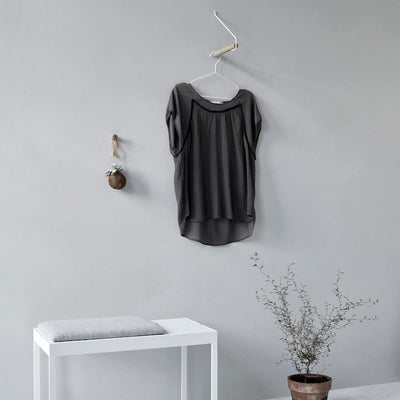 Garderobe "ADD MORE" aus hellbraunem Eichenholz und weißem Metallbügel an Wand mit schwarzer Bluse in Szene
