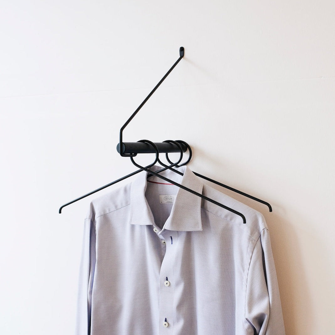Garderobe "ADD MORE" aus schwarzem Eichenholz und schwarzem Metallbügel an Wand mit drei Kleiderhaken in schwarz und blauem Hemd