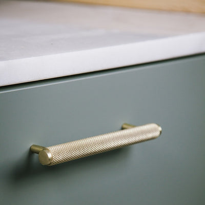 Messing Möbelgriff in kurzer Ausführung horizontal an grünen Küchenunterschrank angebracht.