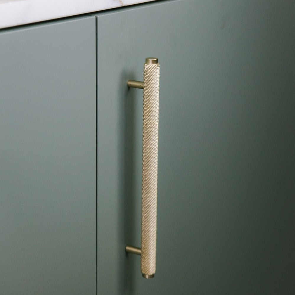 Messing Möbelgriff in langer Ausführung vertikal an grünen Küchenunterschrank angebracht.