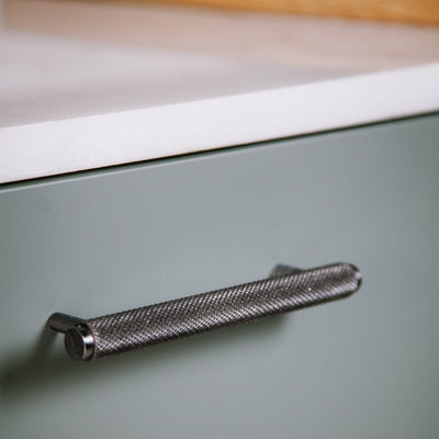 Schwarzer Messing Möbelgriff in kurzer Ausführung horizontal an grünen Küchenunterschrank angebracht.